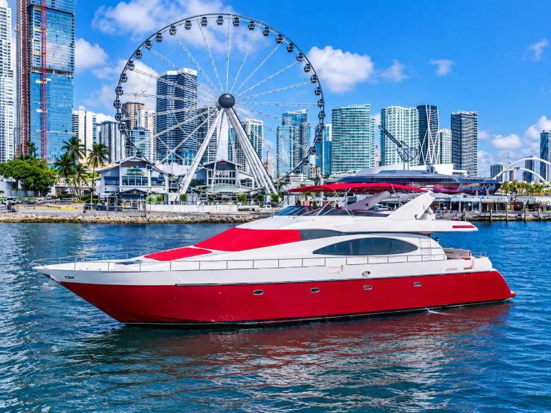 Red and white yacht on water with city skyline and Ferris wheel.