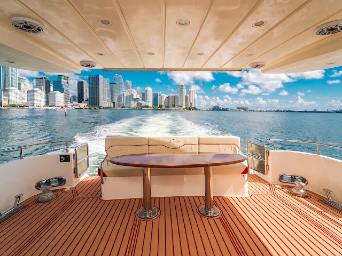 View of city skyline from the back of a yacht with a wooden deck and cushioned seating.