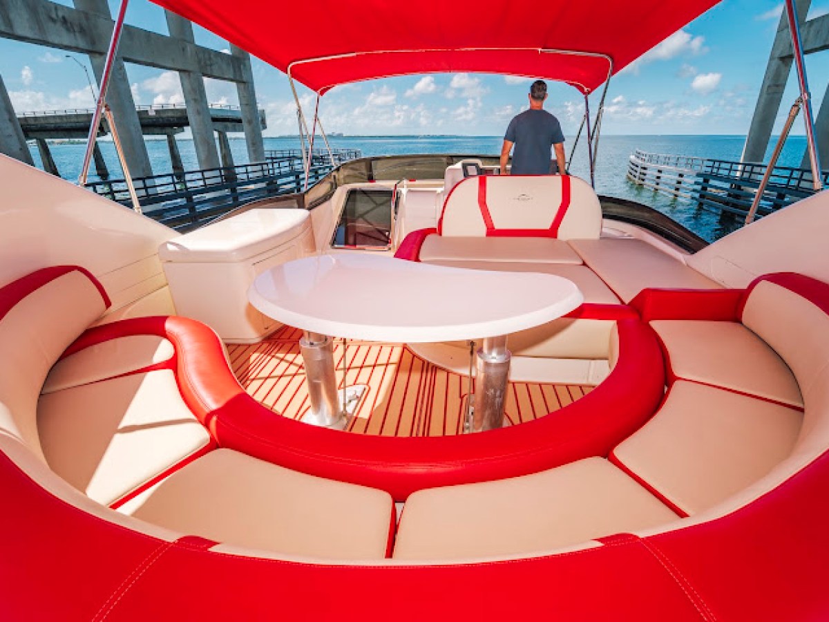 Luxury boat deck with red and beige seating, table, and a person, under a red canopy by the water.